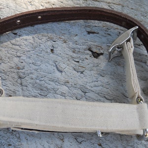 Pu&ograve; includere: Un cinturino in pelle marrone con una sezione in tela color crema e ferramenta in metallo argentato. Il cinturino ha una forma curva ed &egrave; progettato con molteplici punti di attacco.