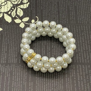 May include: A triple-strand pearl bracelet with a gold-toned clasp. The pearls are white and round.