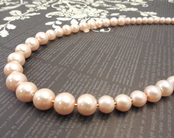 May include: A strand of pale pink faux pearl beads. The pearls are large and round, and the strand is strung on a gold-coloured wire.