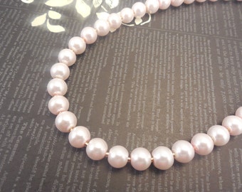 May include: A pink pearl necklace with gold-toned metal spacers. The pearls are large and round, and the necklace is strung on a thin gold chain.