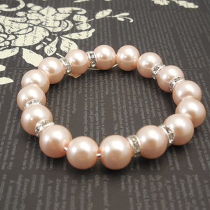May include: A bracelet made of light pink pearls with silver accents. Each pearl is separated by a small silver spacer with rhinestones.