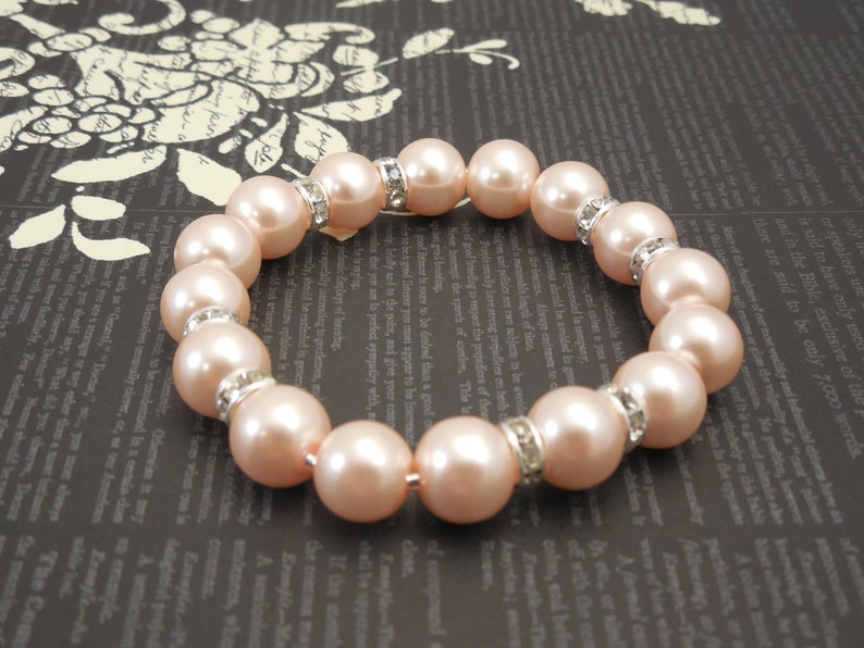 May include: A bracelet made of light pink pearls with silver accents. Each pearl is separated by a small silver spacer with rhinestones.