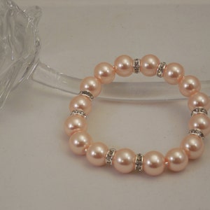 May include: A peach-colored pearl bracelet with silver accents and clear rhinestones.