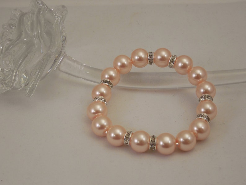 May include: A peach-colored pearl bracelet with silver accents and clear rhinestones.