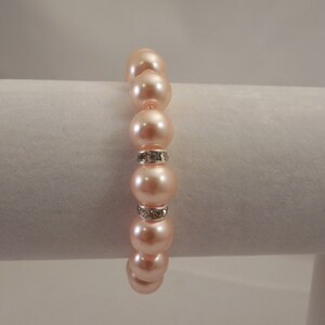 May include: A peach-colored pearl bracelet with a silver rhinestone accent.