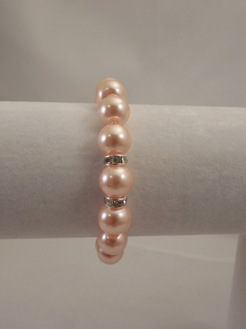 May include: A peach-colored pearl bracelet with a silver rhinestone accent.