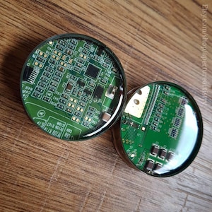 The photo shows our circuit board plugs on a wood style background, the plugs themselves show our bright green circuit board plugs set in a stainless steel plug. The circuit board is intricate in design, and bright green.