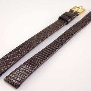 May include: A brown leather watch strap with a gold buckle. The strap has a textured, lizard-like pattern.