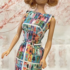 May include: A vintage doll wearing a colorful, patterned dress. The sleeveless dress features a white belt and a print of various figures in different outfits. The doll has red hair and blue eyes.