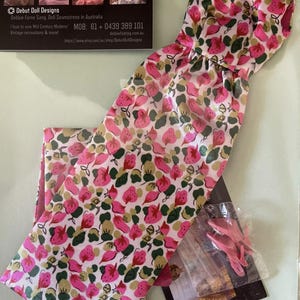 May include: A doll's dress and matching pants set with a pink strawberry pattern on a white background. The dress is strapless with a gathered waist. The image also shows a business card with the text "Debut Doll Designs".
