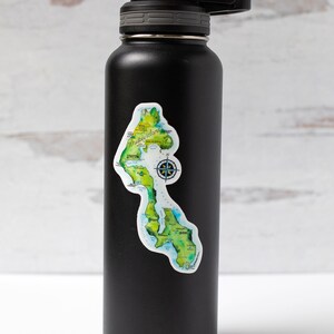 May include: Black insulated water bottle with a sticker of a map of Whidbey Island, Washington. The sticker shows the island's coastline, major towns, and a compass rose.