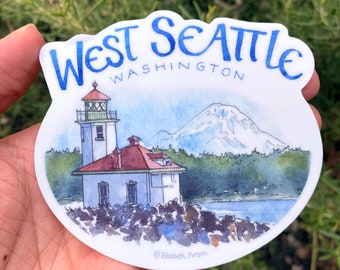 May include: A white sticker with a watercolor illustration of a lighthouse, a mountain, and water. The text "West Seattle Washington" is written in blue cursive at the top of the sticker.