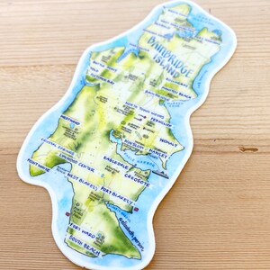 K&ouml;nnte beinhalten: Eine Aquarellkarte von Bainbridge Island, Washington, mit handgeschriebenen Beschriftungen f&uuml;r verschiedene Orte, darunter St&auml;dte, Parks und Str&auml;nde. Die Karte befindet sich auf einem wei&szlig;en Hintergrund mit einem hellblauen Rand.