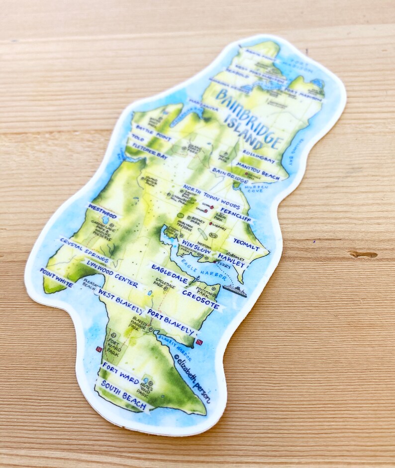 K&ouml;nnte beinhalten: Eine Aquarellkarte von Bainbridge Island, Washington, mit handgeschriebenen Beschriftungen f&uuml;r verschiedene Orte, darunter St&auml;dte, Parks und Str&auml;nde. Die Karte befindet sich auf einem wei&szlig;en Hintergrund mit einem hellblauen Rand.