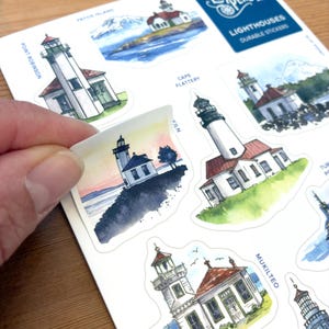 May include: Sheet of durable lighthouse stickers featuring watercolor illustrations. The stickers showcase various lighthouses with white towers, red roofs, and scenic backgrounds of water and sky. The sheet includes the text "Elizabeth Person Art" and lighthouse names.