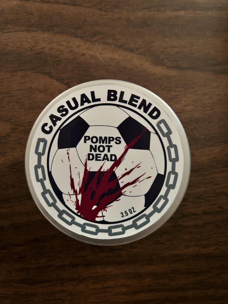 Op de afbeelding: Een ronde metalen blik met een wit deksel voorzien van een zwart-witte voetbalafbeelding, een rood bloedspatontwerp en een grijze kettingrand. De tekst luidt CASUAL BLEND, POMPS NOT DEAD en 3.5 OZ in zwarte letters op de witte achtergrond.