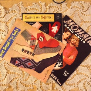 Può includere: Tre libri di modelli di maglia vintage con copertine colorate. Il primo libro presenta un paio di calze con un motivo a rombi, il secondo libro mostra un guanto rosso con un disegno di pupazzo di neve bianco, e il terzo libro presenta una donna con un maglione rosa. I libri sono intitolati "Bear Brand Socks", "Gloves and Mittens", e "Mohair Hand Knits".