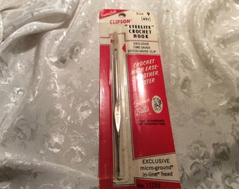 May include: A silver crochet hook with a red and white label. The label reads "Susan Bates Clipson "Steelite" Crochet Hook" and "Exclusive Time-Saver Stitch Saver Clip". The label also says "Crochet with Ease-Other Sister" and "Exclusive micro-ground® in-line® head No. 12205".