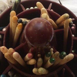 May include: A close-up of a wooden organizer with multiple compartments filled with various colored knitting needles. The organizer is made of dark wood and has a round, raised center.