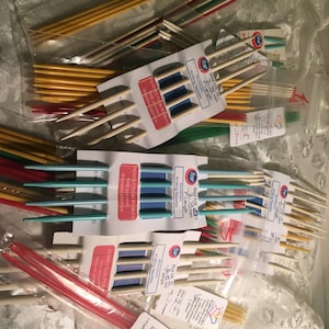 Puede incluir: Una colecci&oacute;n de agujas de tejer de varios tama&ntilde;os y colores, incluyendo rojo, amarillo, azul y verde. Las agujas est&aacute;n empaquetadas en bolsas de pl&aacute;stico transparentes con etiquetas que indican el tama&ntilde;o y el material de las agujas. Las etiquetas tambi&eacute;n incluyen el texto "Bey" y "Perfection Points".