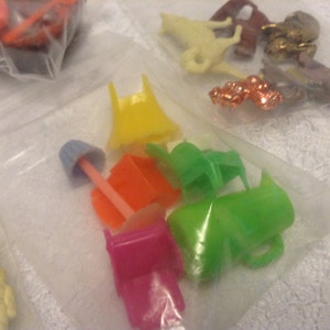 May include: A collection of colorful plastic furniture pieces for a dollhouse, including chairs, a table, and a lamp. The pieces are in various shades of green, yellow, pink, orange, and blue.