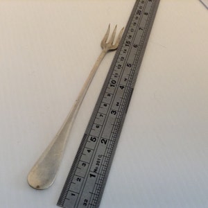 Könnte beinhalten: Eine silberne Gabel mit einem langen Stiel und drei Zinken. Die Gabel wird an einem Lineal gemessen und ist etwa 16,5 cm lang.