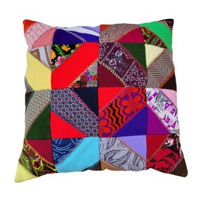 May include: A square throw pillow featuring a patchwork design of various fabric scraps in diverse colors including red, blue, green, yellow, and purple. The pieces are joined by decorative zigzag stitching, creating a complex geometric pattern.