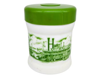 May include: A white glass canister with a glossy green lid. The body of the canister features a detailed green ink illustration of a paddlewheel steamboat on a river, complete with smokestacks, railings, and deck structures against a cloudy sky.