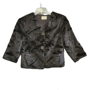 May include: A dark brown, textured jacket with three buttons and two pockets. The jacket has three-quarter sleeves and a notched collar. The jacket is hanging on a clear plastic hanger.