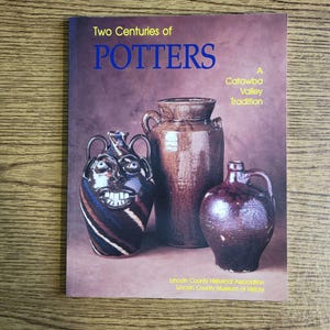 May include: A book titled Two Centuries of POTTERS: A Catawba Valley Tradition by the Lincoln County Historical Association. The cover features three brown ceramic vessels, including a face jug with white teeth, against a brown background.