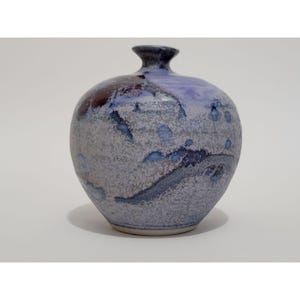 May include: A small, round ceramic vase with a mottled glaze in shades of blue, purple, and white. The vase has a textured surface and a slightly flared opening.