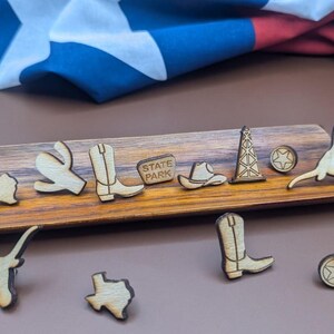 May include: A wooden tray with various wooden cutouts, including a cowboy boot, a cactus, a state park sign, a cowboy hat, a longhorn steer, a star, and a Texas outline. The tray is made of dark wood and has a natural finish.