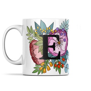 May include: White ceramic mug with a floral design featuring a large pink flower and the letter "E" in black. The flowers are in shades of pink, red, yellow, and blue.