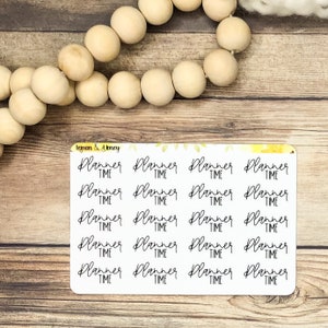 Puede incluir: Una hoja de pegatinas para planificador con las palabras "Planner Time" en una fuente manuscrita. Las pegatinas son blancas con texto negro. La imagen también incluye cuentas de madera y una superficie de madera.