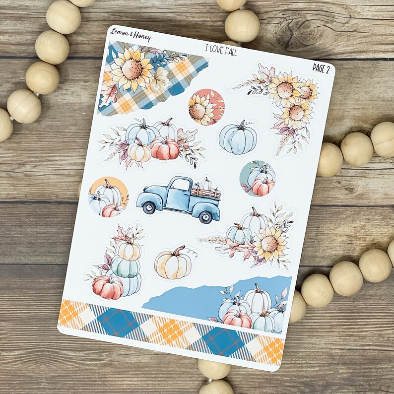 May include: A sheet of fall-themed planner stickers with watercolor illustrations. Designs include pumpkins, sunflowers, a blue truck, and plaid patterns. The text "I LOVE FALL" and "PAGE 2" are visible.