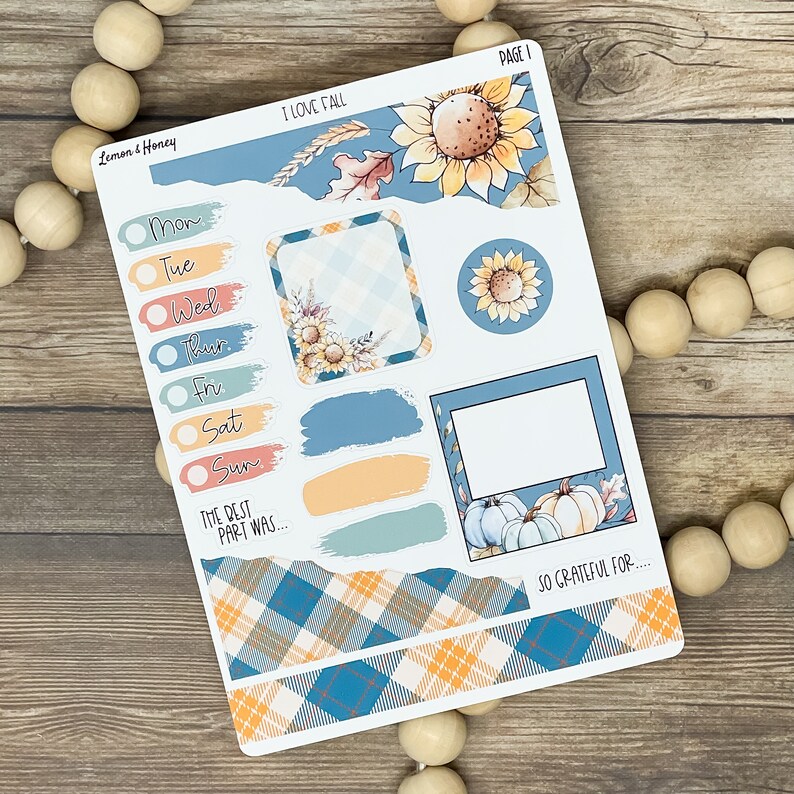 May include: A planner sticker sheet with a fall theme. It features sunflowers, pumpkins, and plaid patterns in shades of blue, orange, and yellow. The sheet includes labels for each day of the week and decorative elements.
