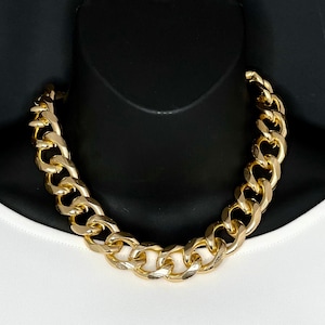 May include: A thick gold chain necklace with large, chunky links. The necklace is made of a shiny metal and has a classic curb chain design.