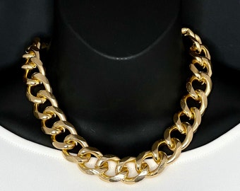 May include: A thick gold chain necklace with large, chunky links. The necklace is made of a shiny metal and has a classic curb chain design.