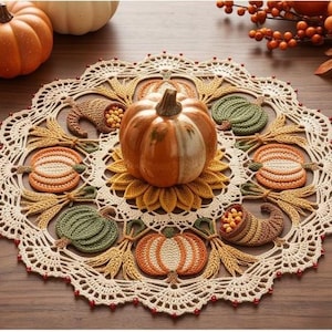 May include: A round, cream-colored crochet doily featuring an intricate lace border with small red beads. The center displays a ceramic orange pumpkin surrounded by crocheted motifs of pumpkins, cornucopias, and wheat stalks in autumn colors.