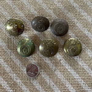 May include: Seven antique brass buttons with the words "CANADA" and "ROYAL" printed on them. The buttons have a raised design of a maple leaf and a crown. A Canadian penny is included for size comparison.