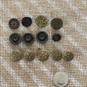 Könnte beinhalten: Eine Sammlung von 14 Vintage-Knöpfen in verschiedenen Gold- und Brauntönen. Die Knöpfe haben unterschiedliche Designs, darunter florale, geometrische und Wirbelmuster. Die Knöpfe sind in einem Rastermuster auf einem Jute-Hintergrund angeordnet.