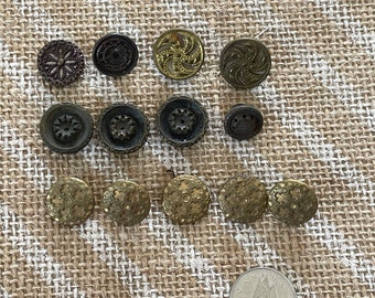 以下が含まれることがあります： 金色と茶色の様々な色合いのヴィンテージボタン14個のセット。ボタンは、花柄、幾何学模様、渦巻き模様など、様々なデザインが施されています。ボタンは、麻布の背景にグリッドパターンで配置されています。
