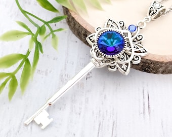 May include: A silver key necklace with a blue iridescent crystal set in a filigree design. The key is attached to a silver chain.