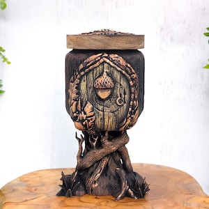 May include: A wooden box with a tree bark design and a copper acorn on the front. The box is shaped like a goblet and has a lid.