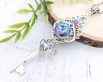 May include: A silver key necklace with a large iridescent blue crystal and smaller purple crystals. The key is ornate and has a filigree design.