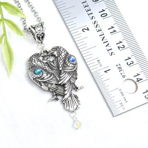May include: Silver necklace with a pendant of two intertwined owls with blue and green crystal accents. The pendant is about 1 1/2 inches tall.