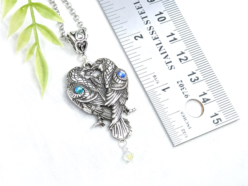 May include: Silver necklace with a pendant of two intertwined owls with blue and green crystal accents. The pendant is about 1 1/2 inches tall.