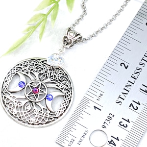 May include: Silver necklace with a triple moon pendant featuring a pentagram with a red gemstone and blue crystals. The pendant is approximately 1.5 inches in diameter.