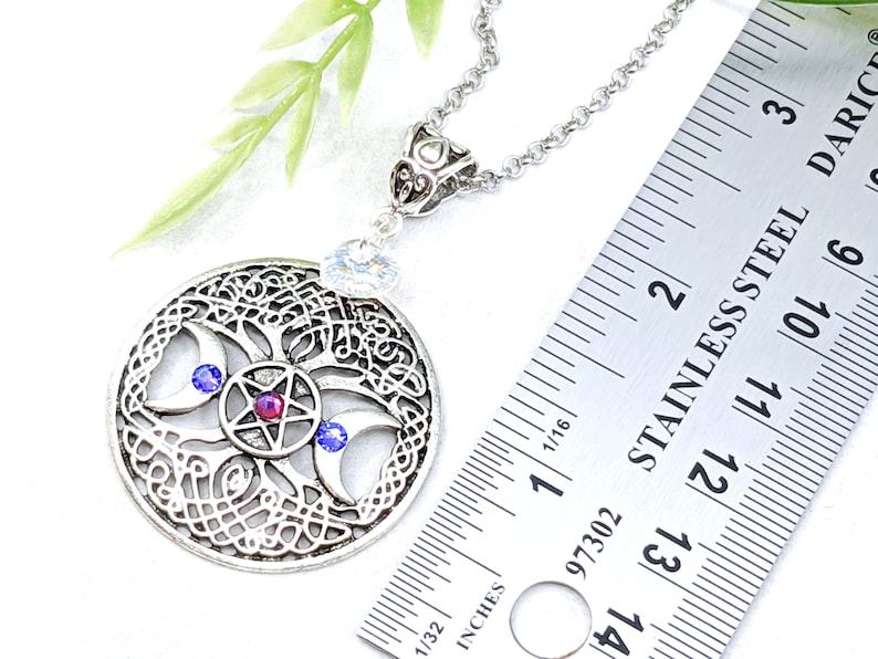 May include: Silver necklace with a triple moon pendant featuring a pentagram with a red gemstone and blue crystals. The pendant is approximately 1.5 inches in diameter.
