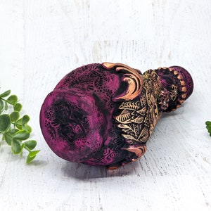 May include: A pink and gold ceramic vase with intricate floral designs. The vase is decorated with gold accents and has a textured surface.